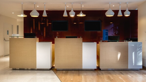 Zona de recepción con diseño moderno, que presenta un mostrador de madera, varias lámparas colgantes y un televisor de pantalla plana montado en la pared.