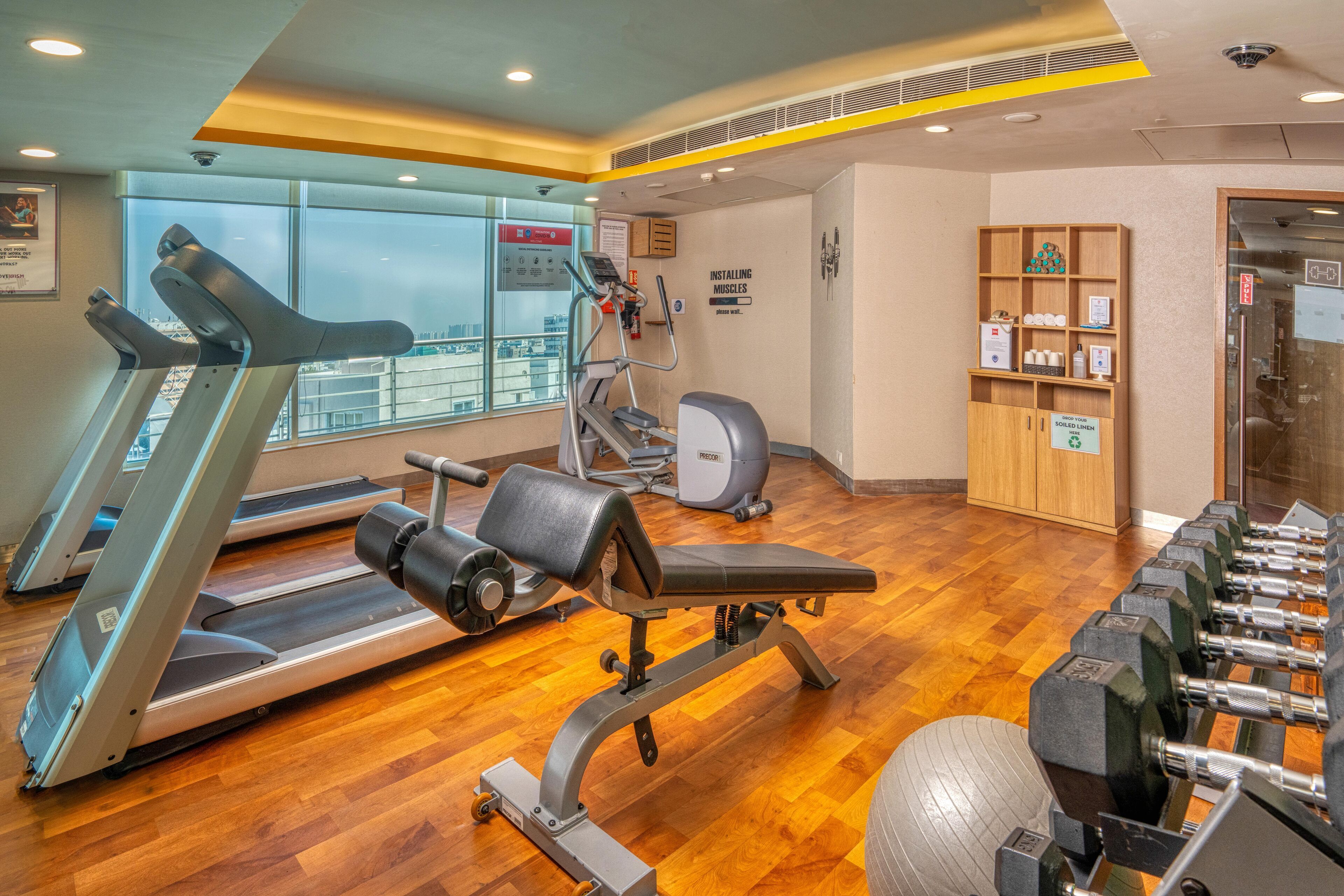 Un gimnasio con cintas de correr, una bicicleta estática, un banco y un juego de mancuernas.