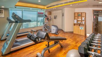 Un gimnasio con cintas de correr, una bicicleta estática, un banco y un juego de mancuernas.
