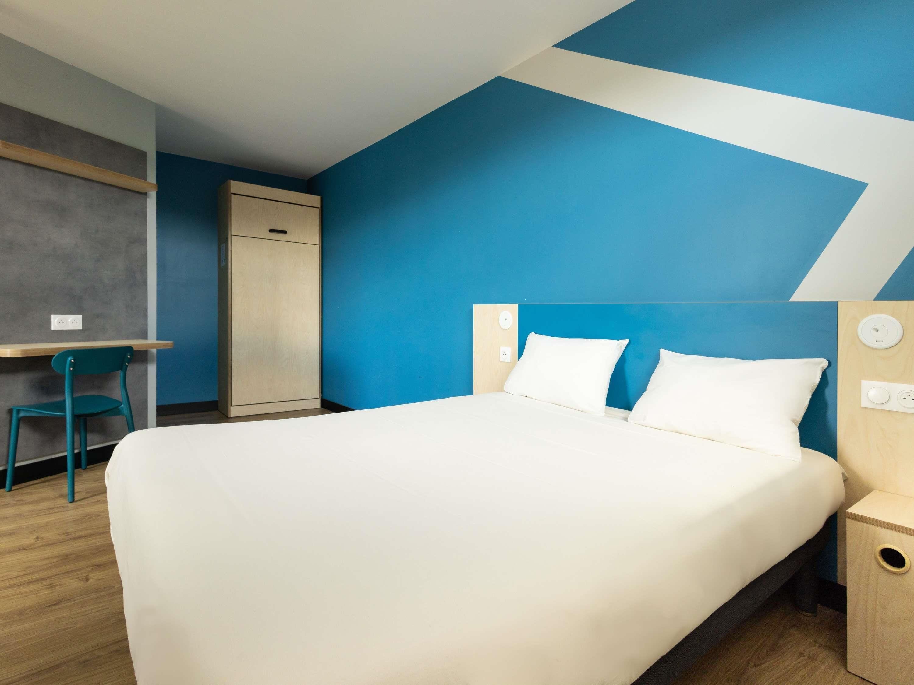 Une chambre d’hôtel moderne équipée d’un lit, d’un bureau, d’une chaise et d’une armoire.