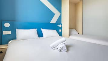 Una habitación de hotel con una cama grande, dos almohadas, una toalla doblada con cuidado y un armario de madera.