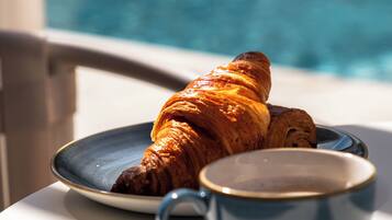 A croissant on a plate next to a cup, with a pool in the background.