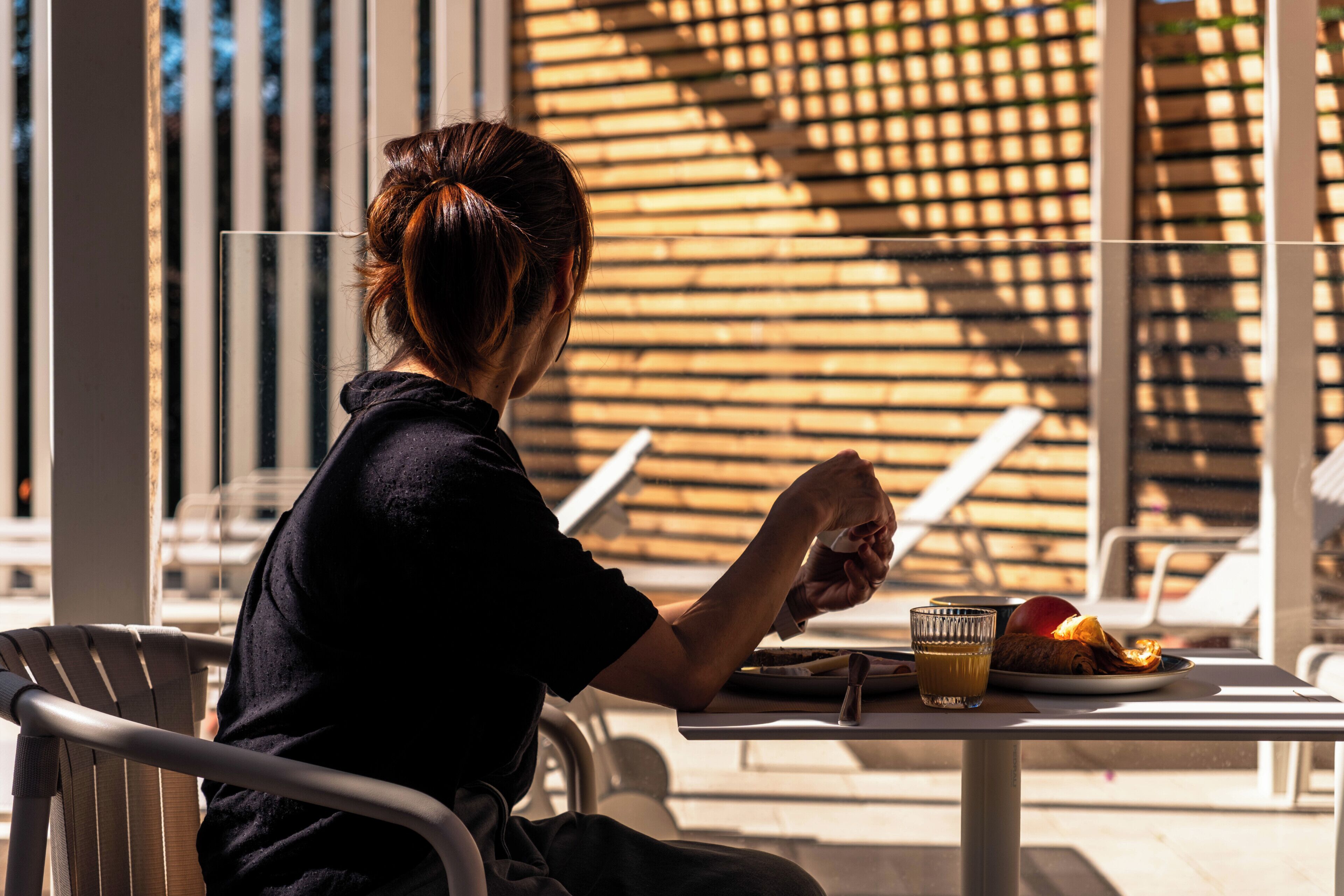 A person seated at an outdoor table with a plate of food, a glass of juice, and a napkin.