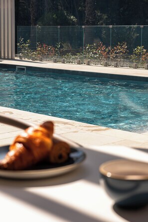 Un cadre agréable au bord de la piscine, avec une assiette de nourriture, un verre et une vue dégagée sur la piscine.