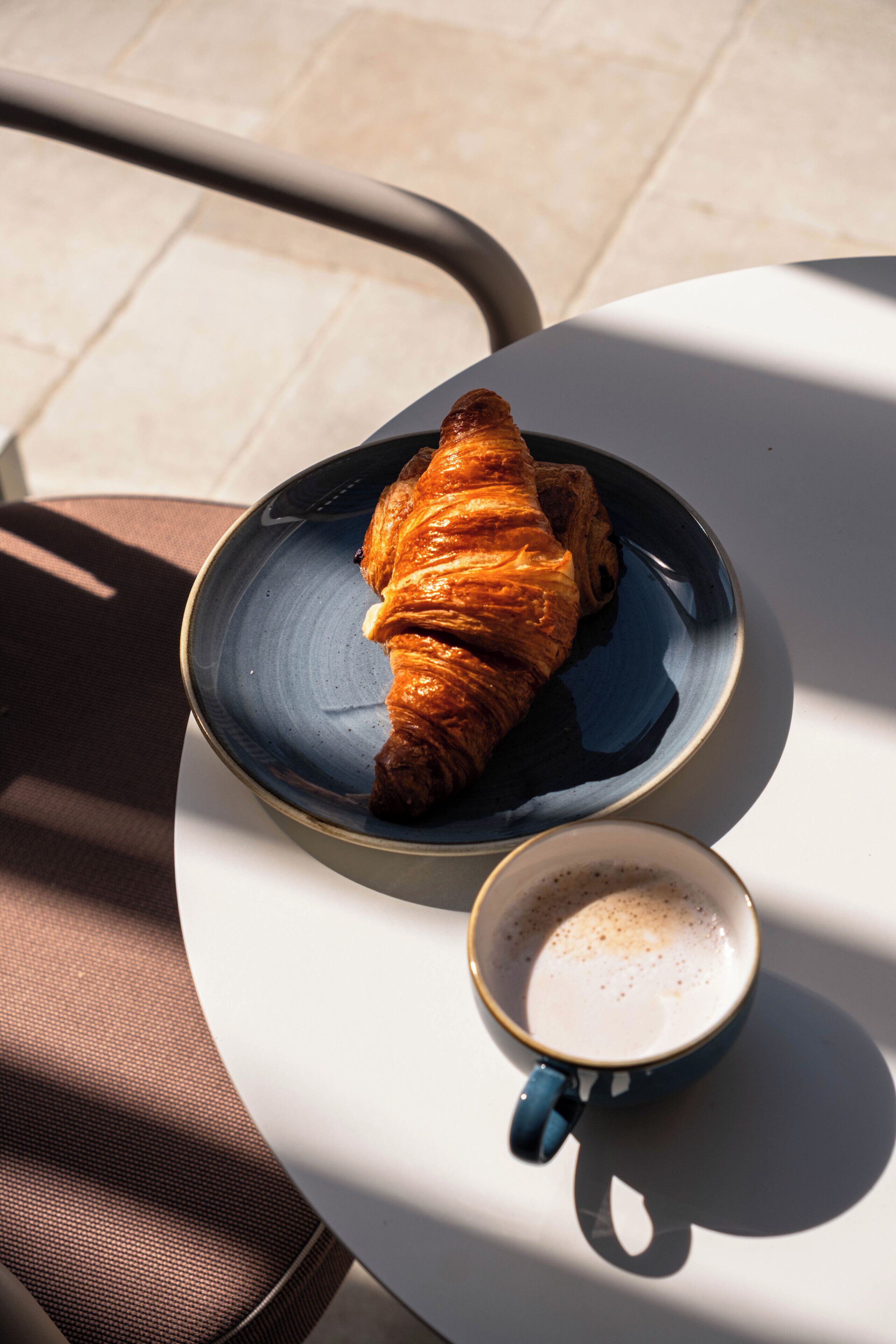 Un croissant en un plato junto a una taza de café sobre una mesa.