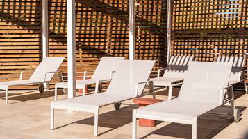 A sunlit outdoor seating area with white lounge chairs and a wooden lattice wall in the background.