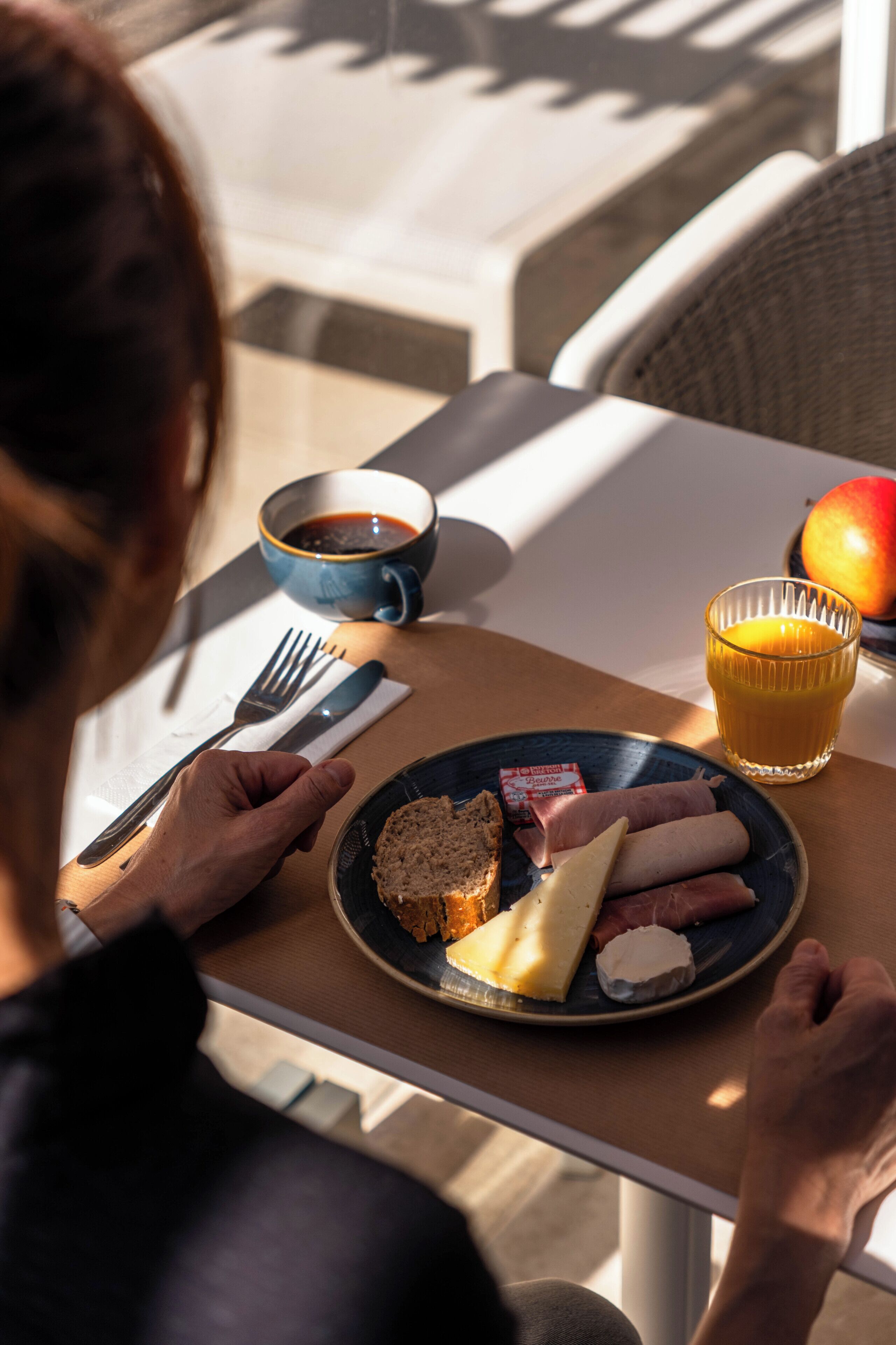 A person seated at a table with a plate of food, a cup of coffee, and a glass of orange juice.