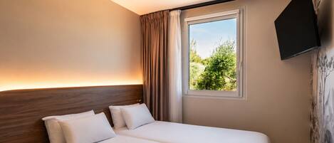 A hotel room with two beds, a window with curtains, a mounted TV, and a wall with a nature-themed mural.