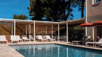 A swimming pool with lounge chairs and umbrellas, surrounded by a wooden pergola and trees.