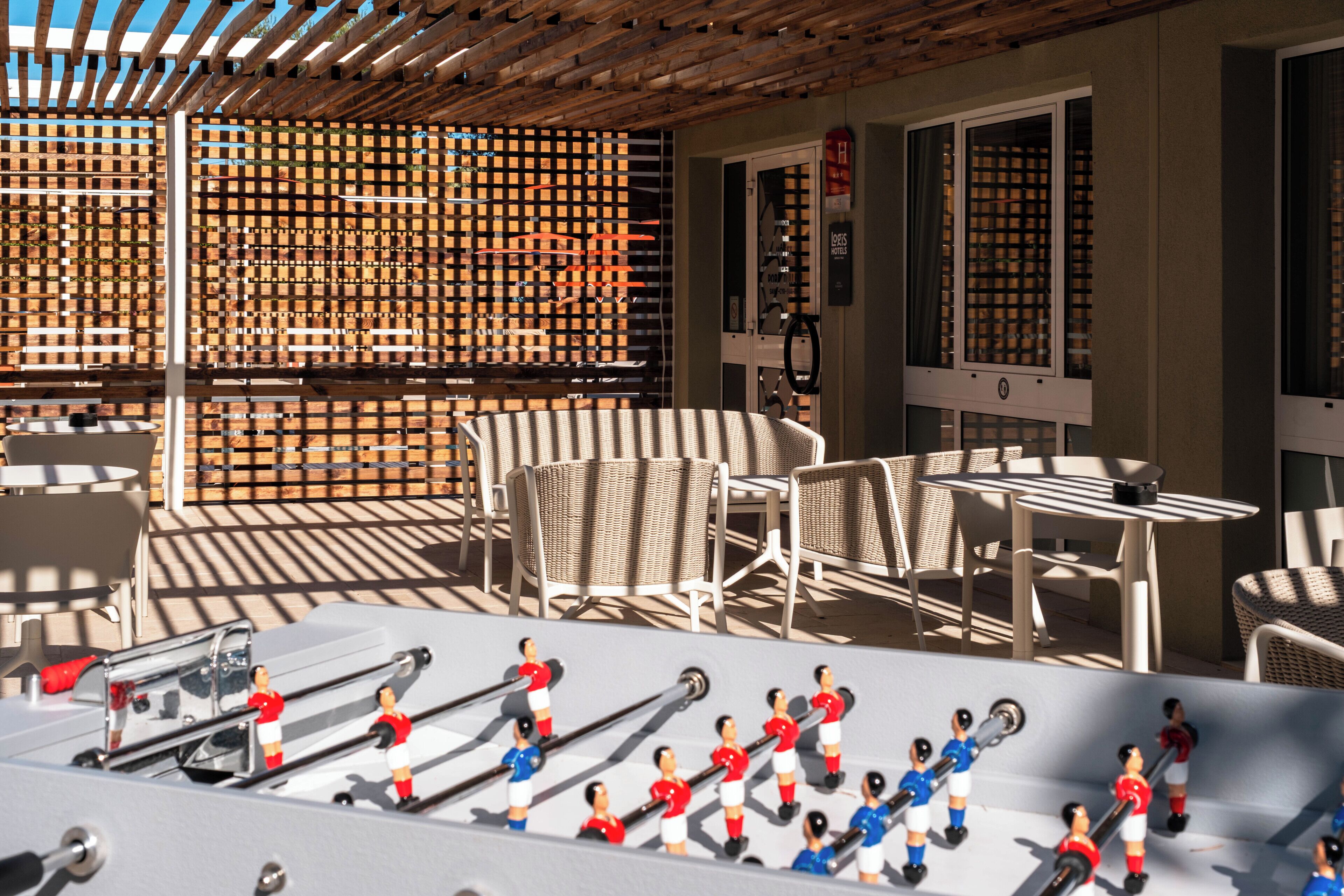 Un patio con mobiliario exterior, una mesa de futbolín y una estructura de pérgola de madera.