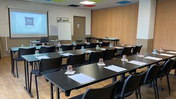 A conference room with a projector screen, whiteboard, and tables with chairs.