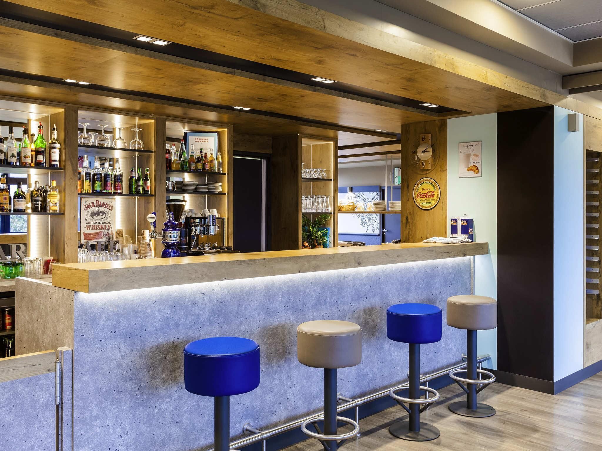 Una zona de bar con mostrador, taburetes, estantes con botellas y un cartel de whisky Jack Daniel's.