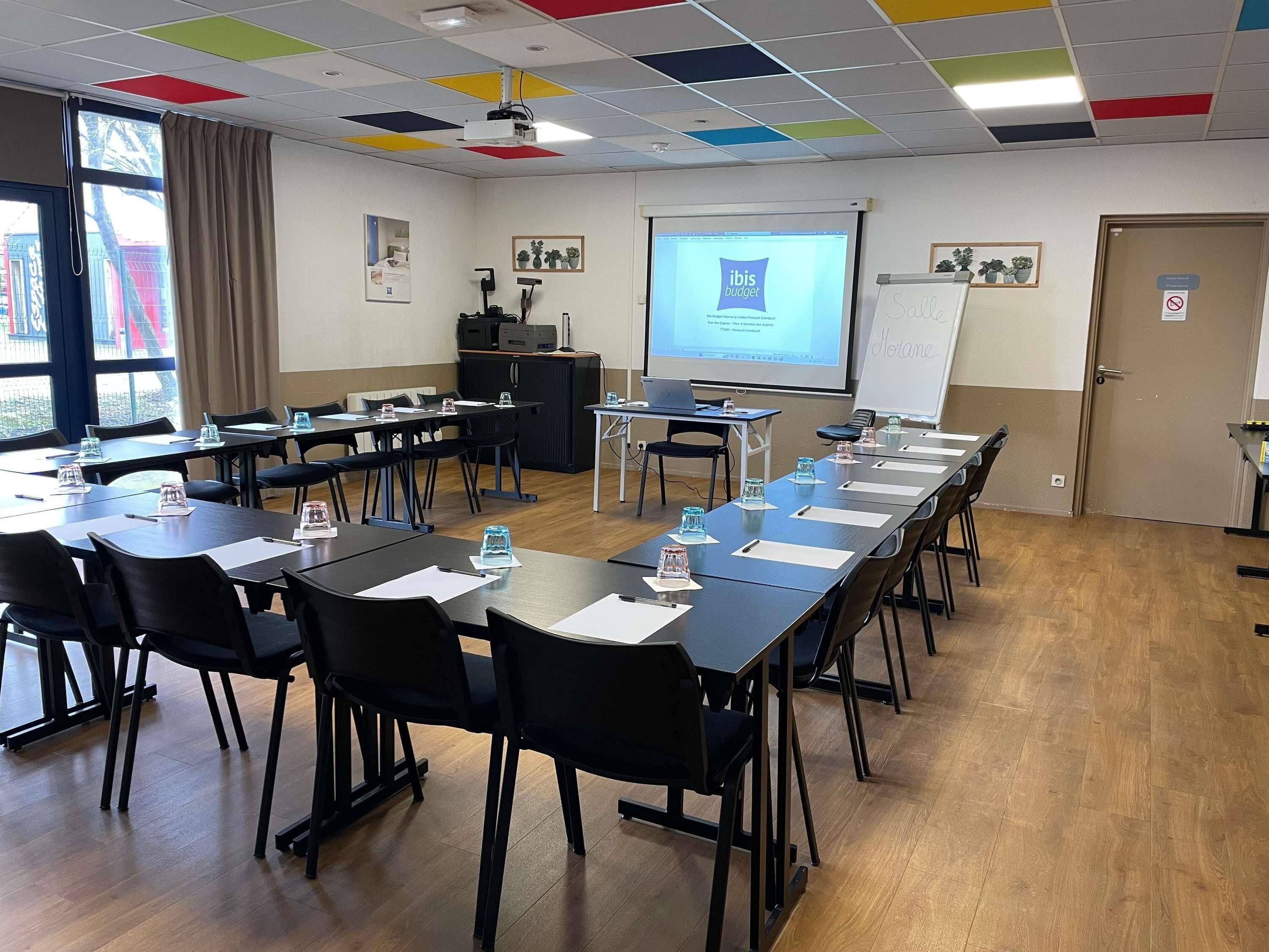 A conference room with a long table, chairs, a projector screen, and a whiteboard.