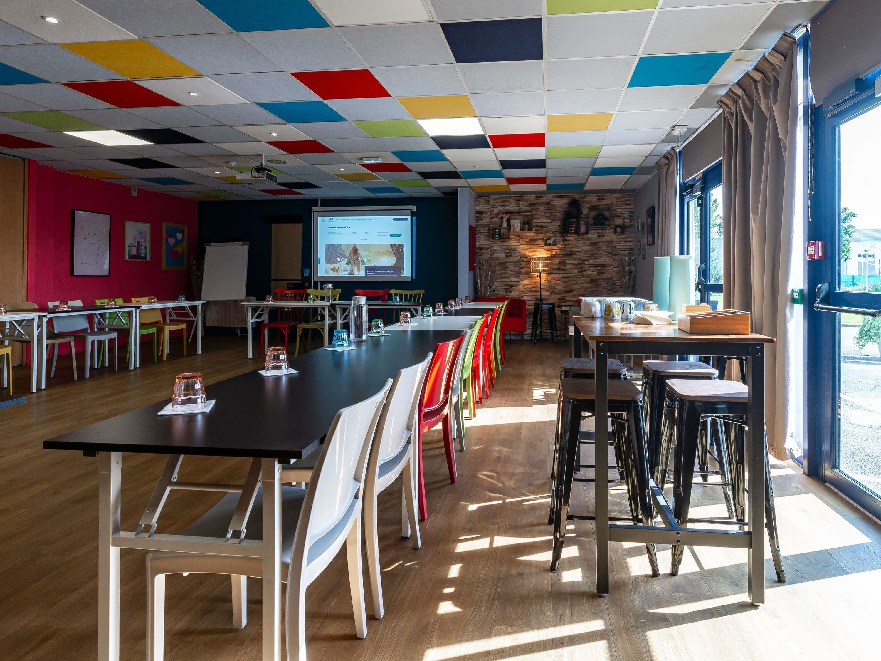 A conference room with a long table, chairs, a projector screen, and a stone wall.