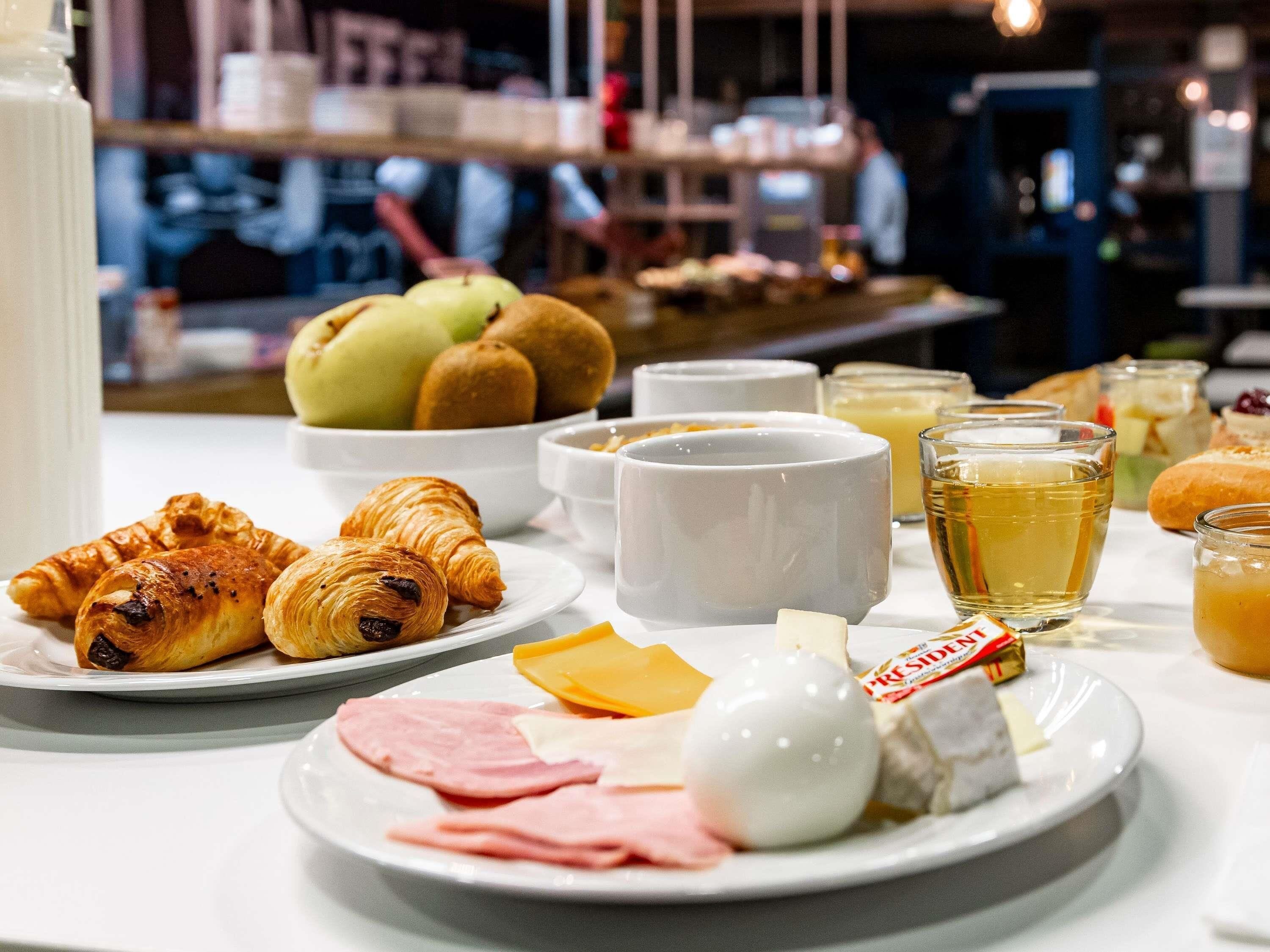 Un bufé de desayuno con cruasanes, queso, jamón y una variedad de frutas y bebidas.