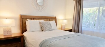 Un lit bien fait, avec du linge de lit blanc et des oreillers à rayures, deux lampes de chevet et un miroir fixé au mur.