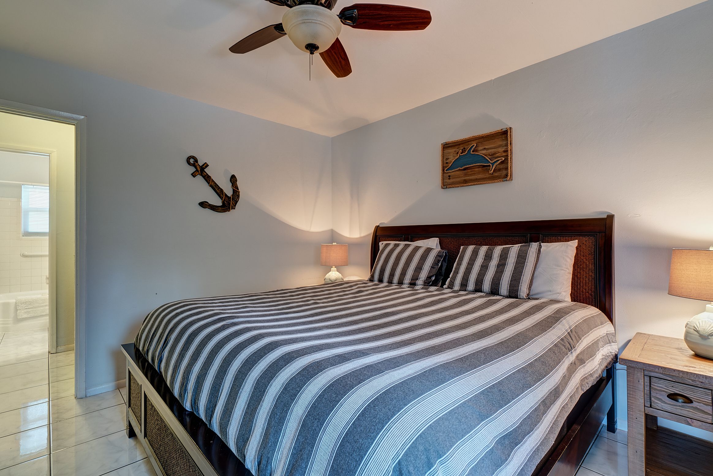 A neatly made bed with striped bedding, a wooden headboard, a nightstand with a lamp, and a ceiling fan.