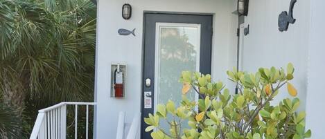A staircase leading to a door with a fish sign, a potted plant, and a fire extinguisher on the wall.