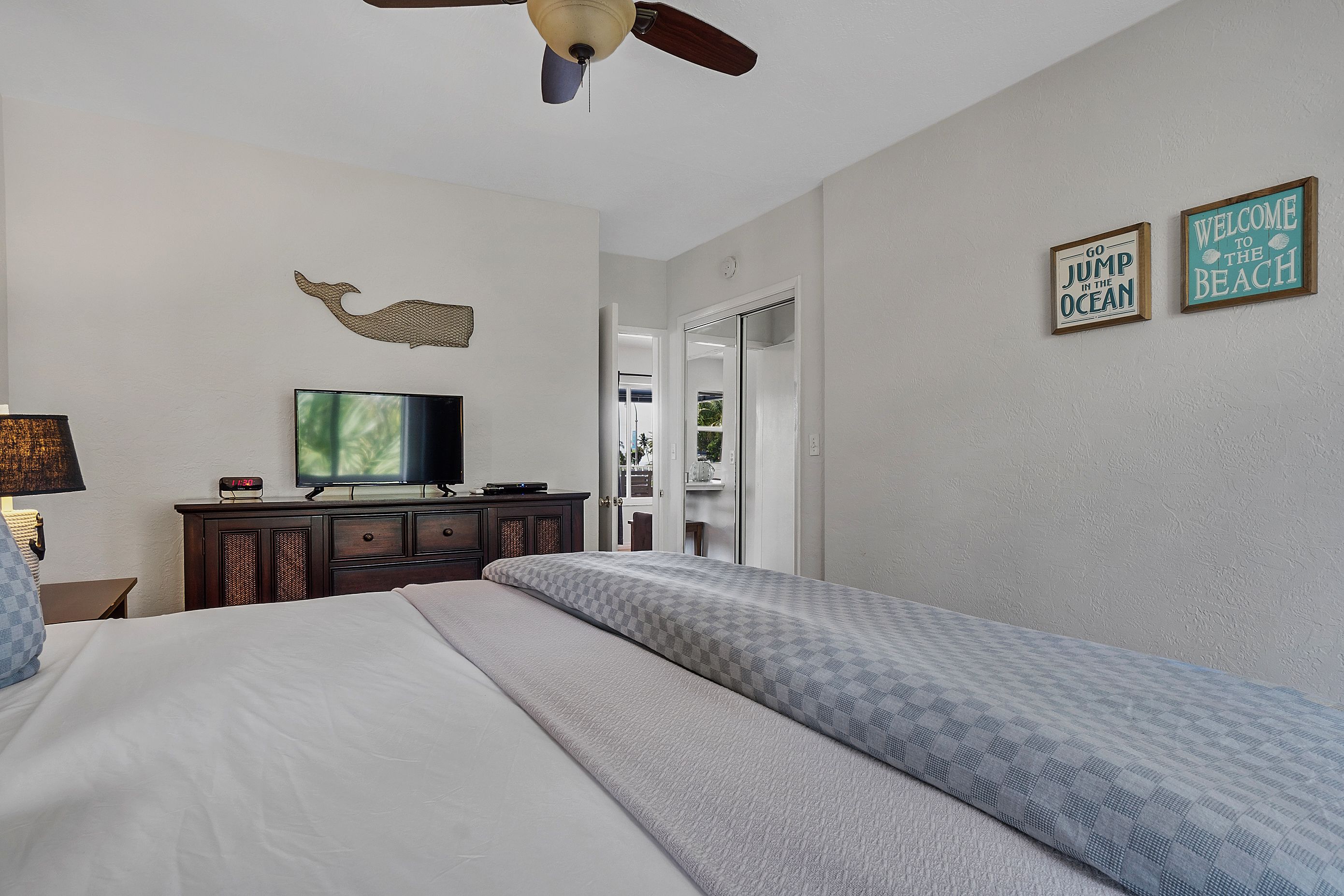 A hotel room with a bed, a television, a ceiling fan, and two wall decorations.