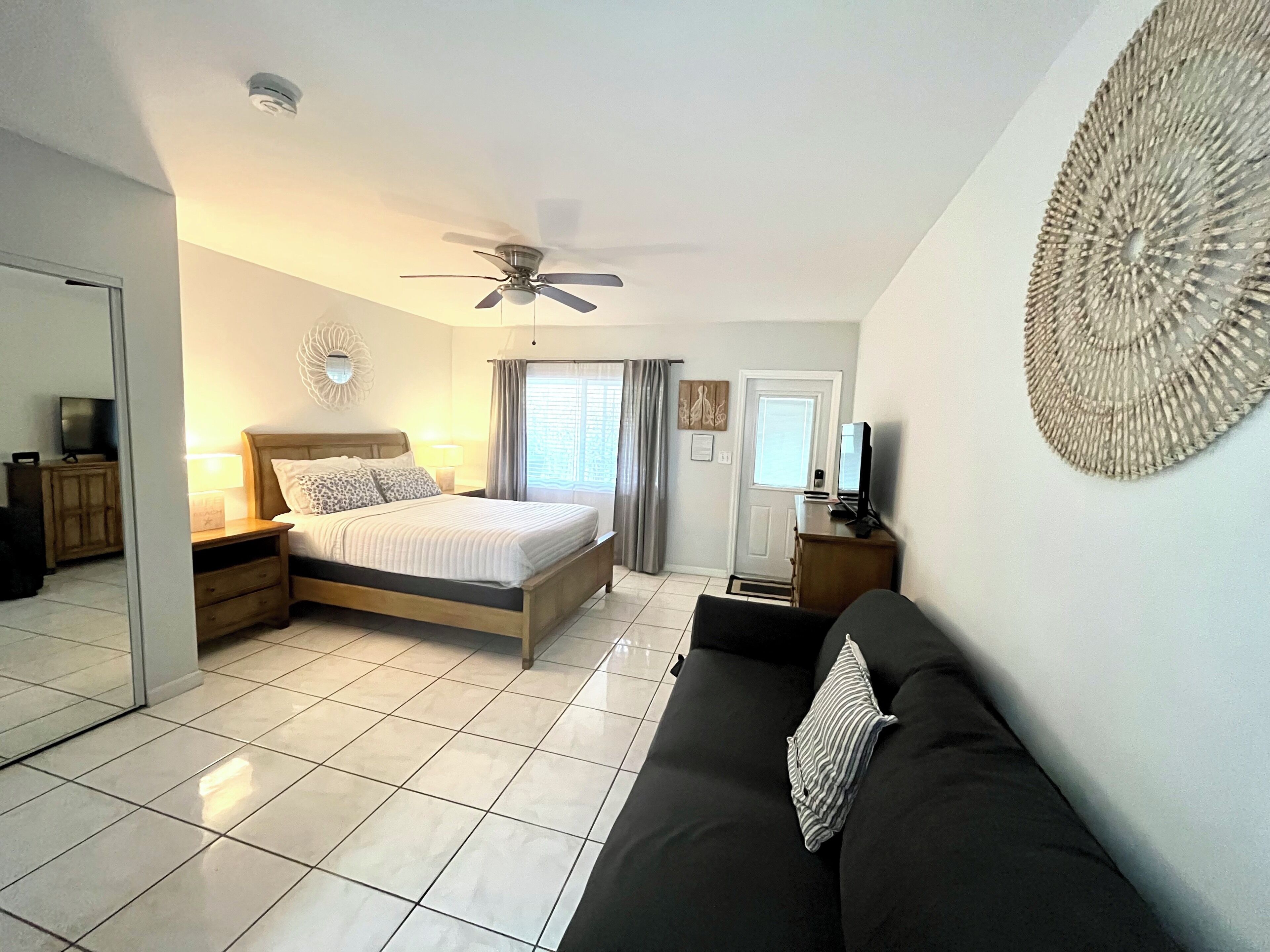 Une chambre à coucher avec un lit, un ventilateur de plafond, une télévision, un canapé et une porte.