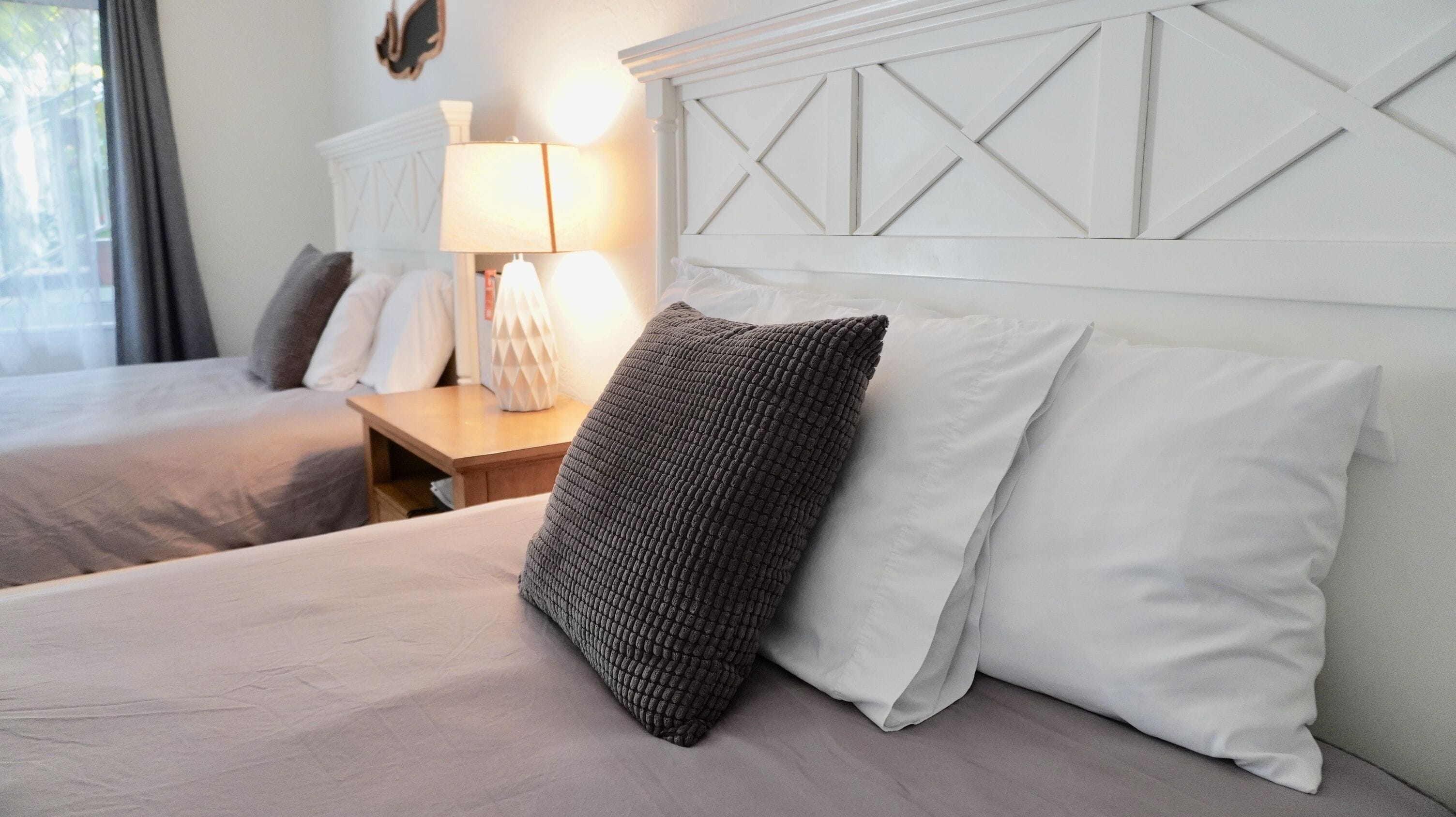 Habitación de hotel con dos camas, una mesita de noche con lámpara y un cabecero decorativo.