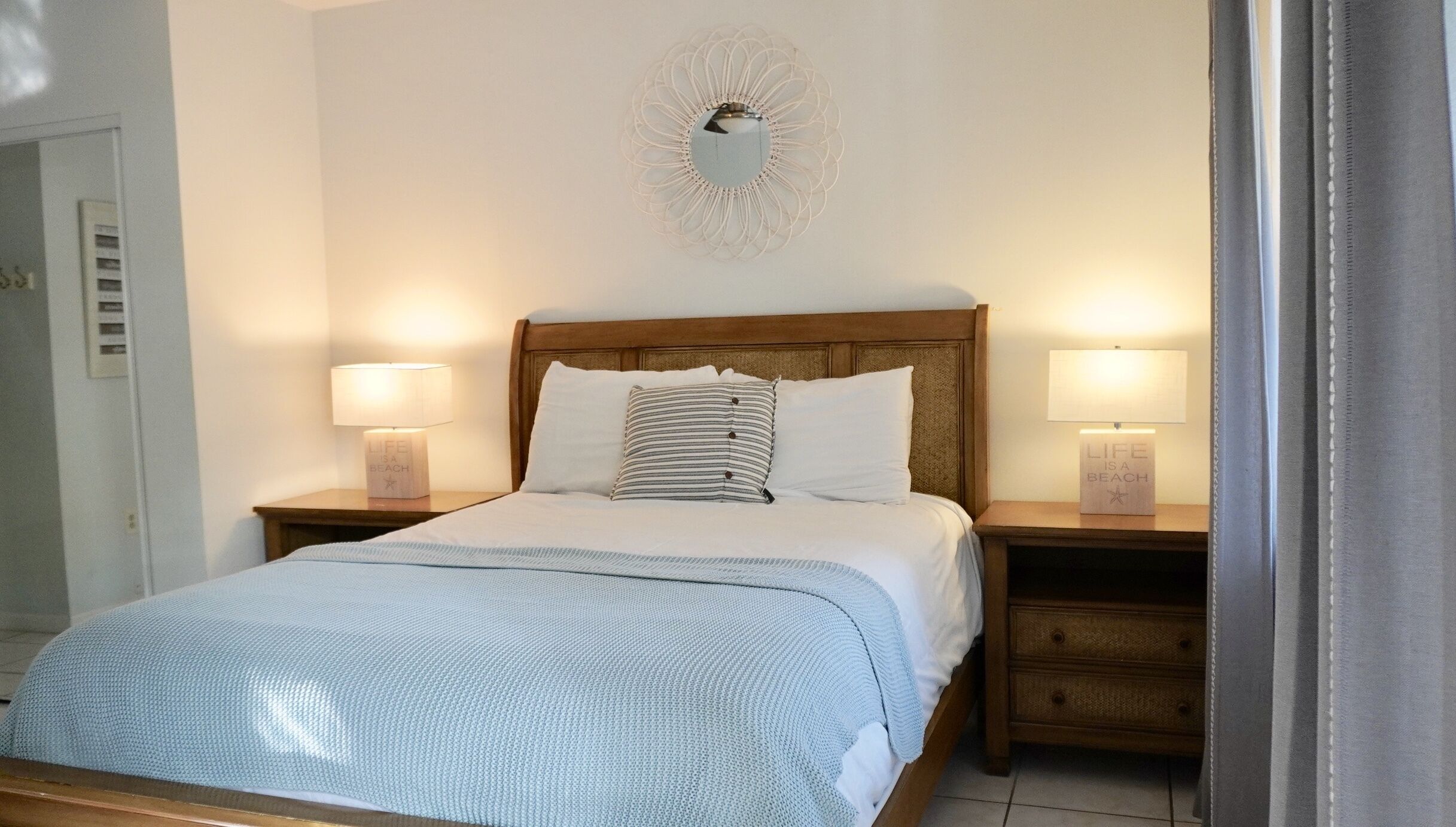 A neatly made bed with a striped pillow, two bedside lamps, and a decorative wall piece above the bed.