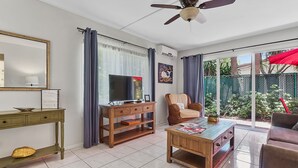 Ein Wohnzimmer mit Fernseher, Deckenventilator, Sofa, Couchtisch und einem Fenster mit Vorhängen.