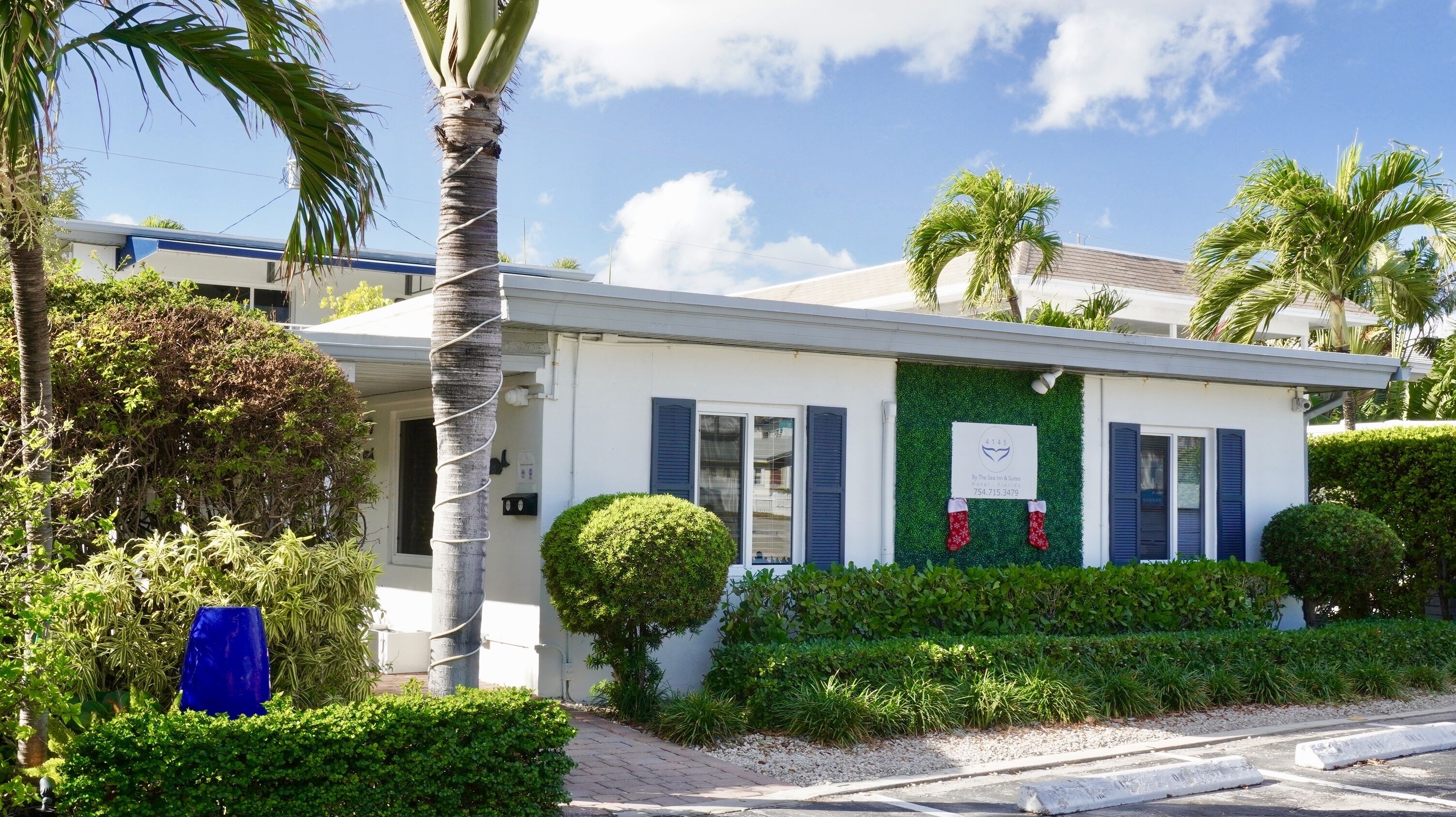 A white building with a green wall and blue shutters, surrounded by lush greenery and palm trees.