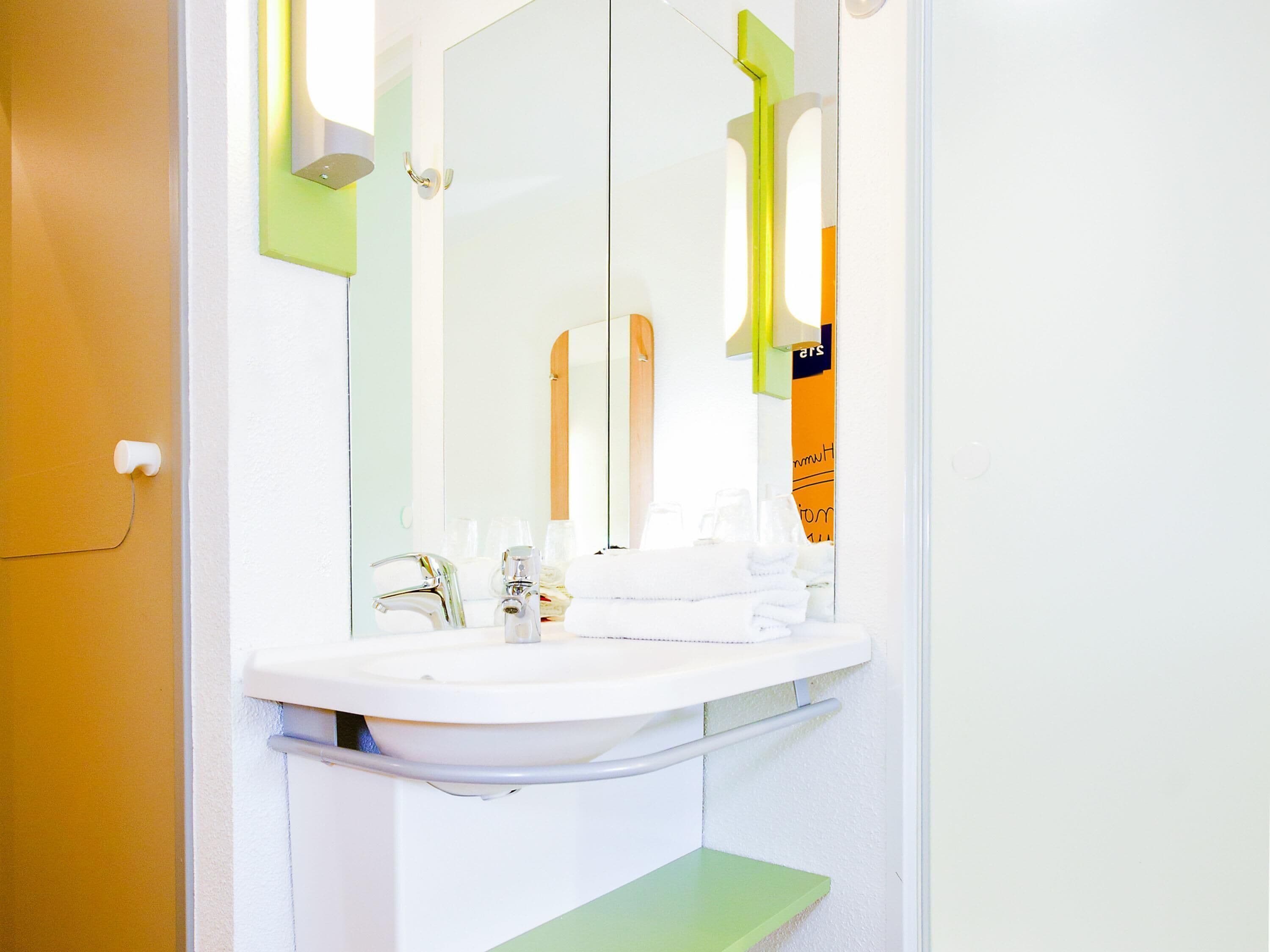 Un baño con lavamanos blanco, espejo y detalles verdes en la pared.