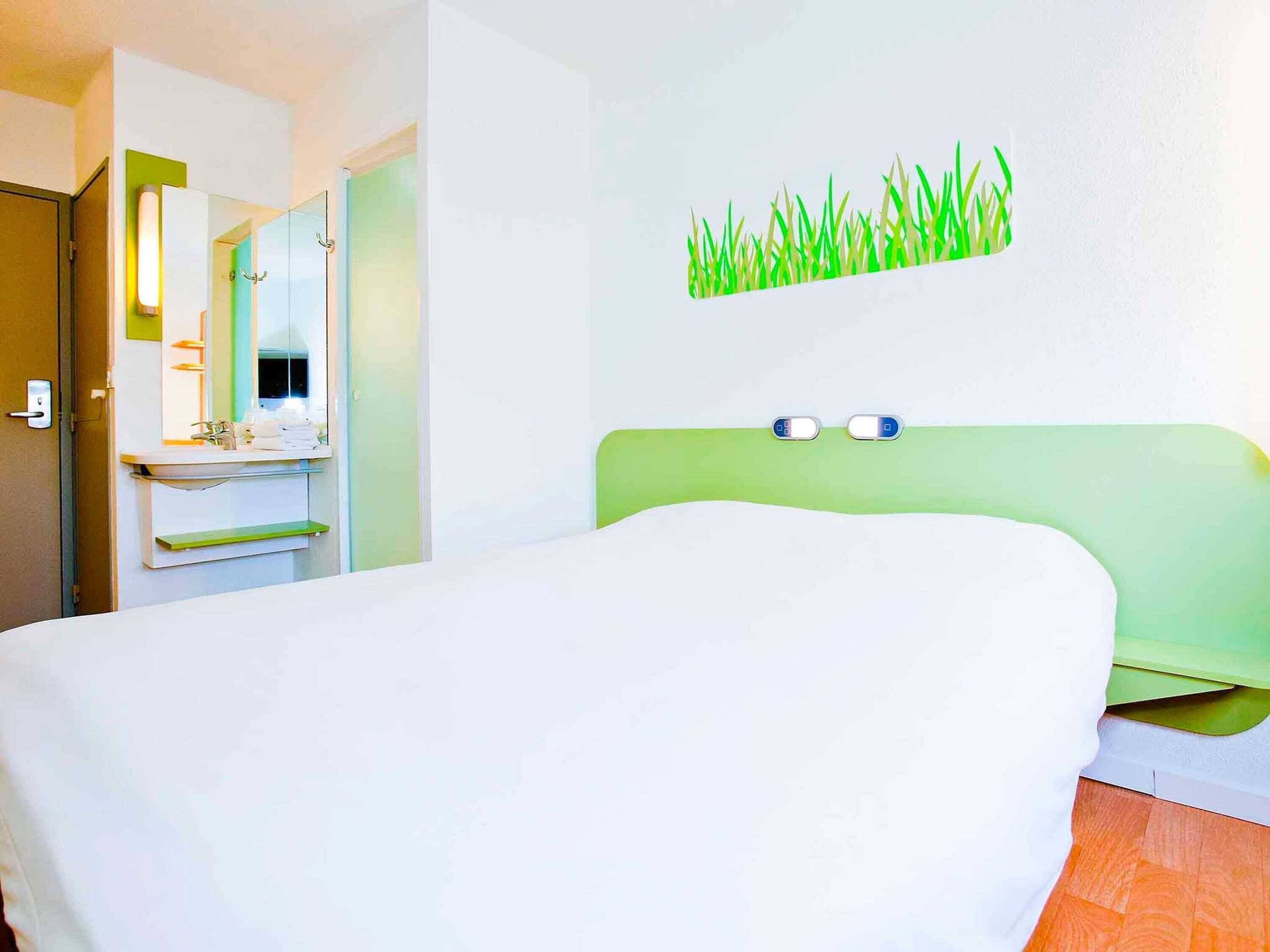 Habitación de hotel con cama, baño con espejo y decoración de pared verde.