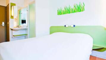 Habitación de hotel con cama, baño con espejo y decoración de pared verde.
