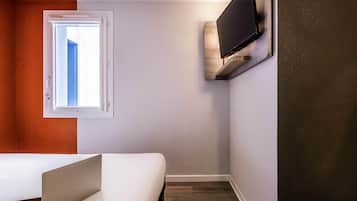 Una stanza con un letto, una finestra, una TV a parete e un portatile sul tavolo.