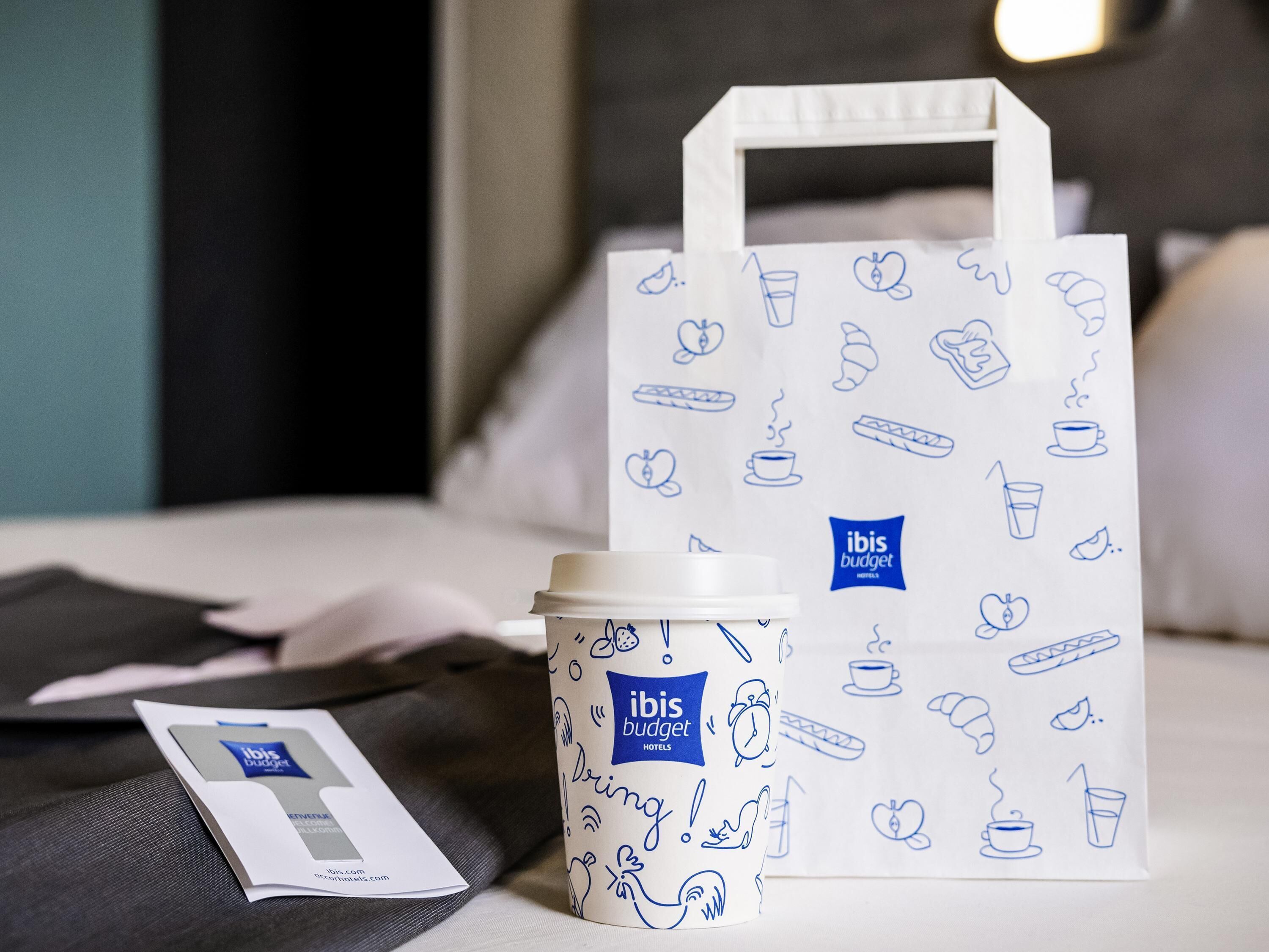 Une chambre d'hôtel avec un lit, un sac blanc orné de motifs bleus, et une tasse à café.
