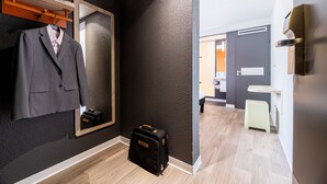 A hotel room with a mirror, a suit hanging, a suitcase, and a small stool. - ibis budget Perpignan Sud (Perpignan)
