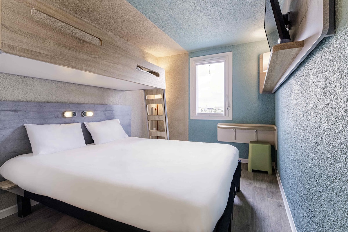 Une chambre d’hôtel moderne équipée d’un lit, d’étagères intégrées, d  ’une fenêtre et d’un téléviseur à écran plat.
