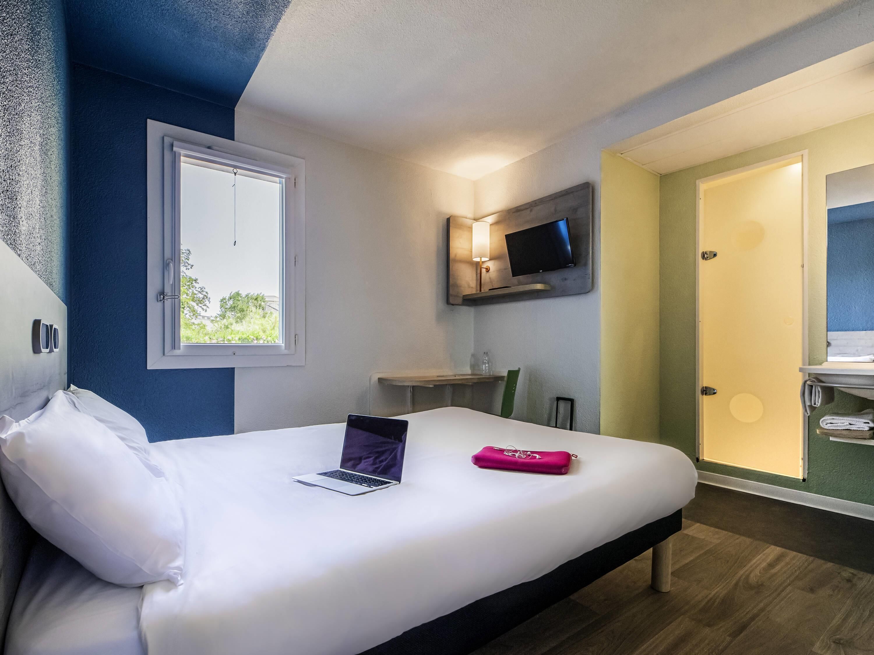 Una habitación de hotel con cama, escritorio, televisor y ventana.