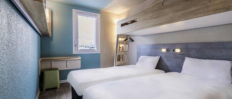A hotel room with two beds, a window, a built-in shelf, and a wall-mounted light fixture.