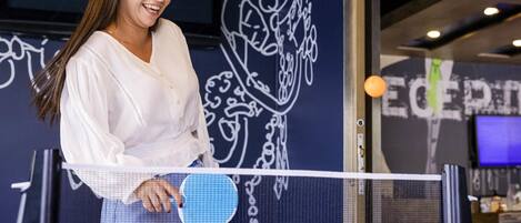 A person holding a paddle, standing in front of a table tennis table with a wall featuring abstract designs in the background.