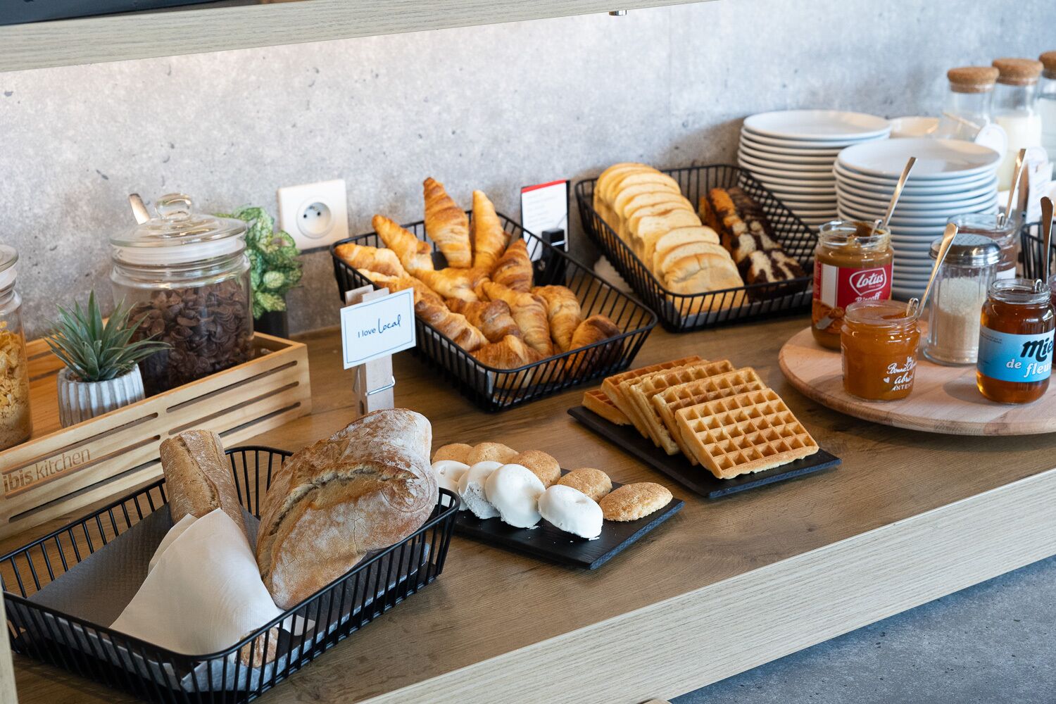 A breakfast buffet with various breads, pastries, waffles, and condiments.