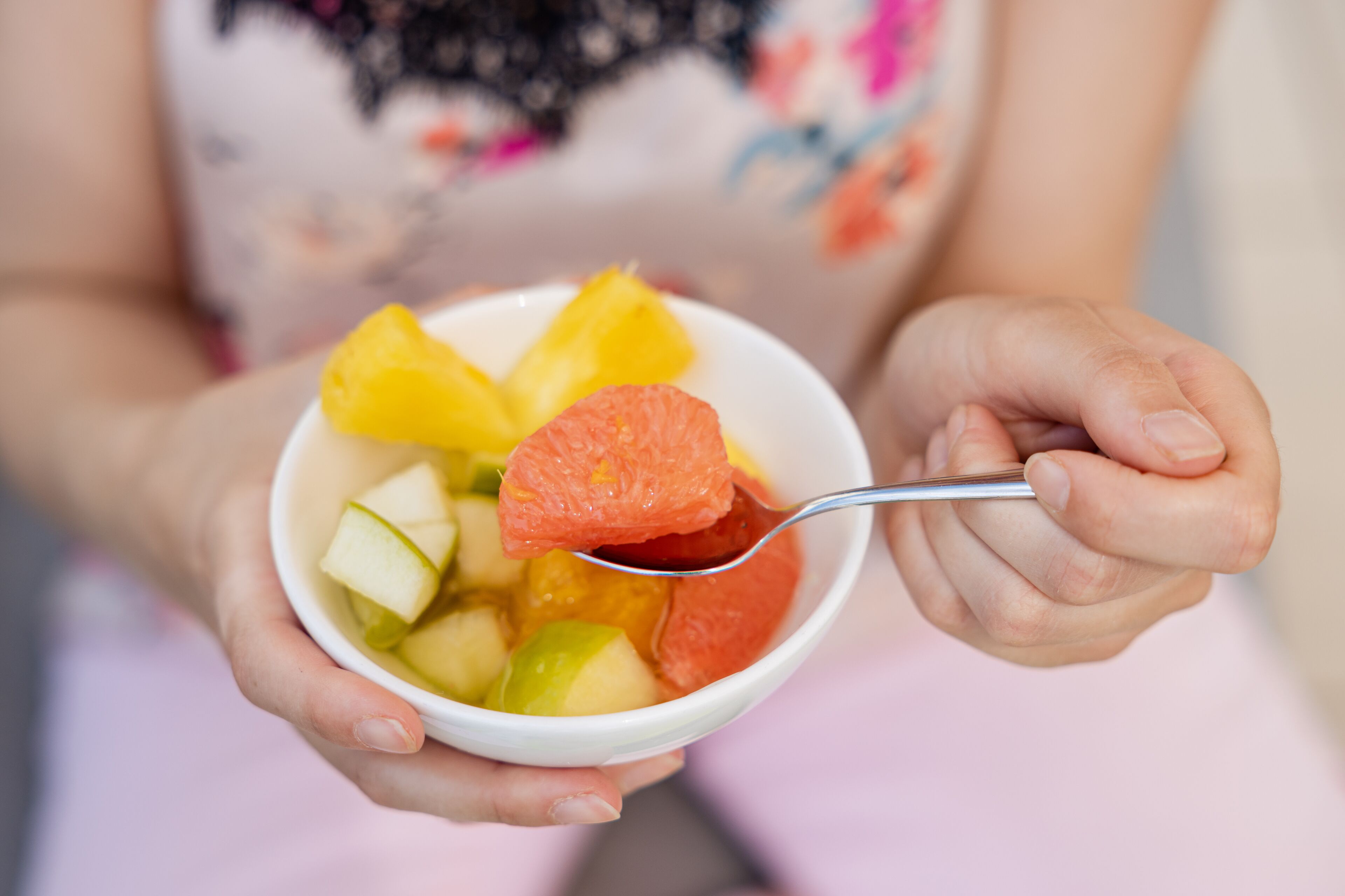 Iemand houdt een fruitsalade in een kom vast, met een lepel.