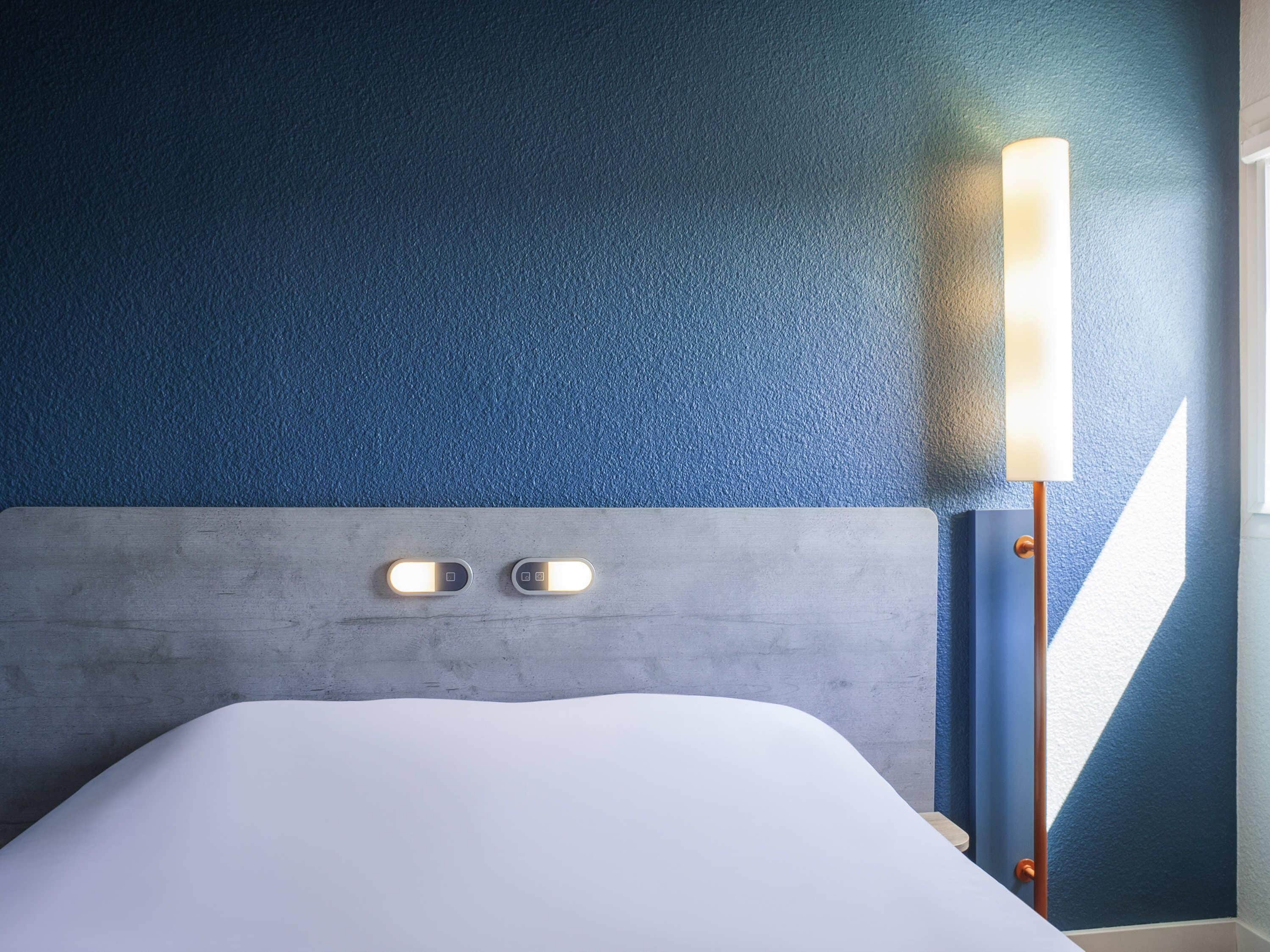 Et hotelværelse med en seng, en sengegavl og en lampe på væggen.