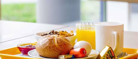 Ein Frühstücksbrett mit Brot, Eiern, einem Muffin, einem Glas Orangensaft und einer Tasse.