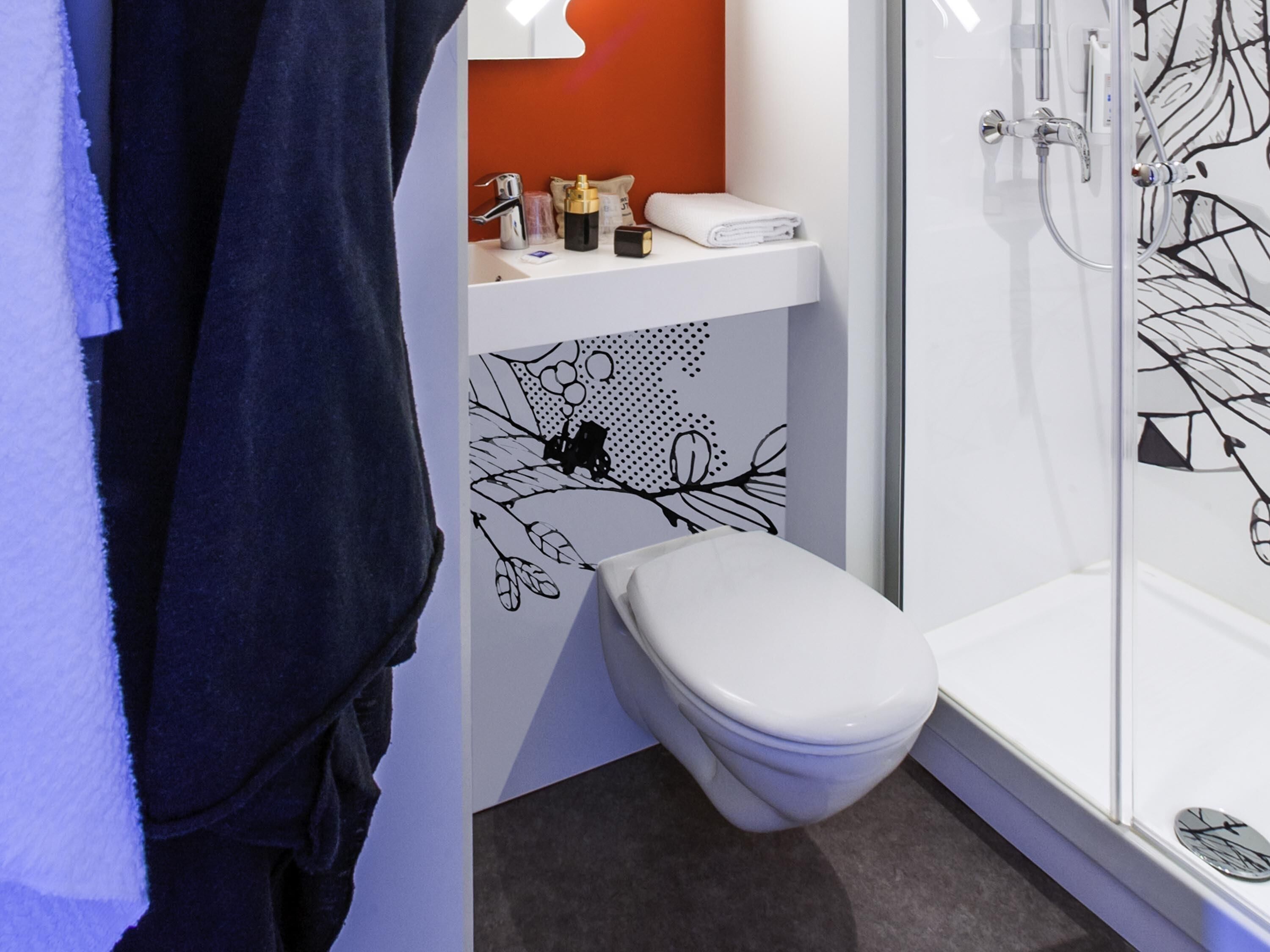 A modern bathroom with a white toilet, a shower area, and a sink with a decorative wall.