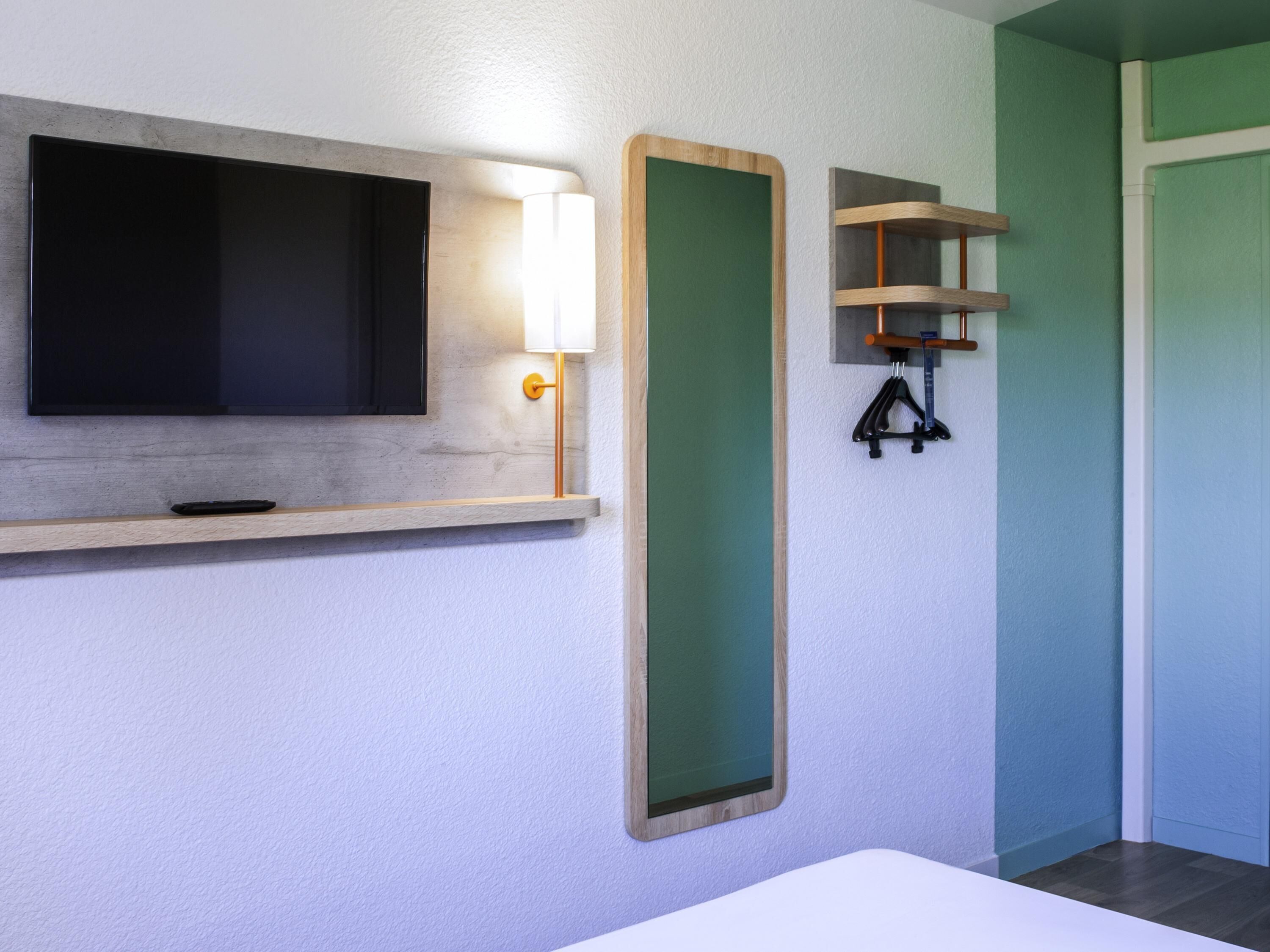 Un baño moderno con una televisión instalada, una luz adosada a la pared y un estante de madera.
