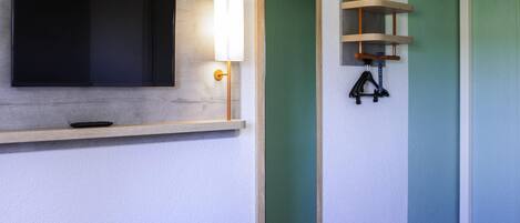 Un baño moderno con una televisión instalada, una luz adosada a la pared y un estante de madera.