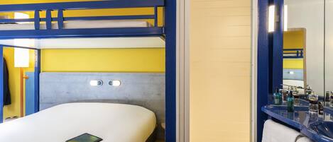 A bunk bed with a headboard, a bedside table with a camera and a tablet, and a bathroom with a mirror and toiletries.