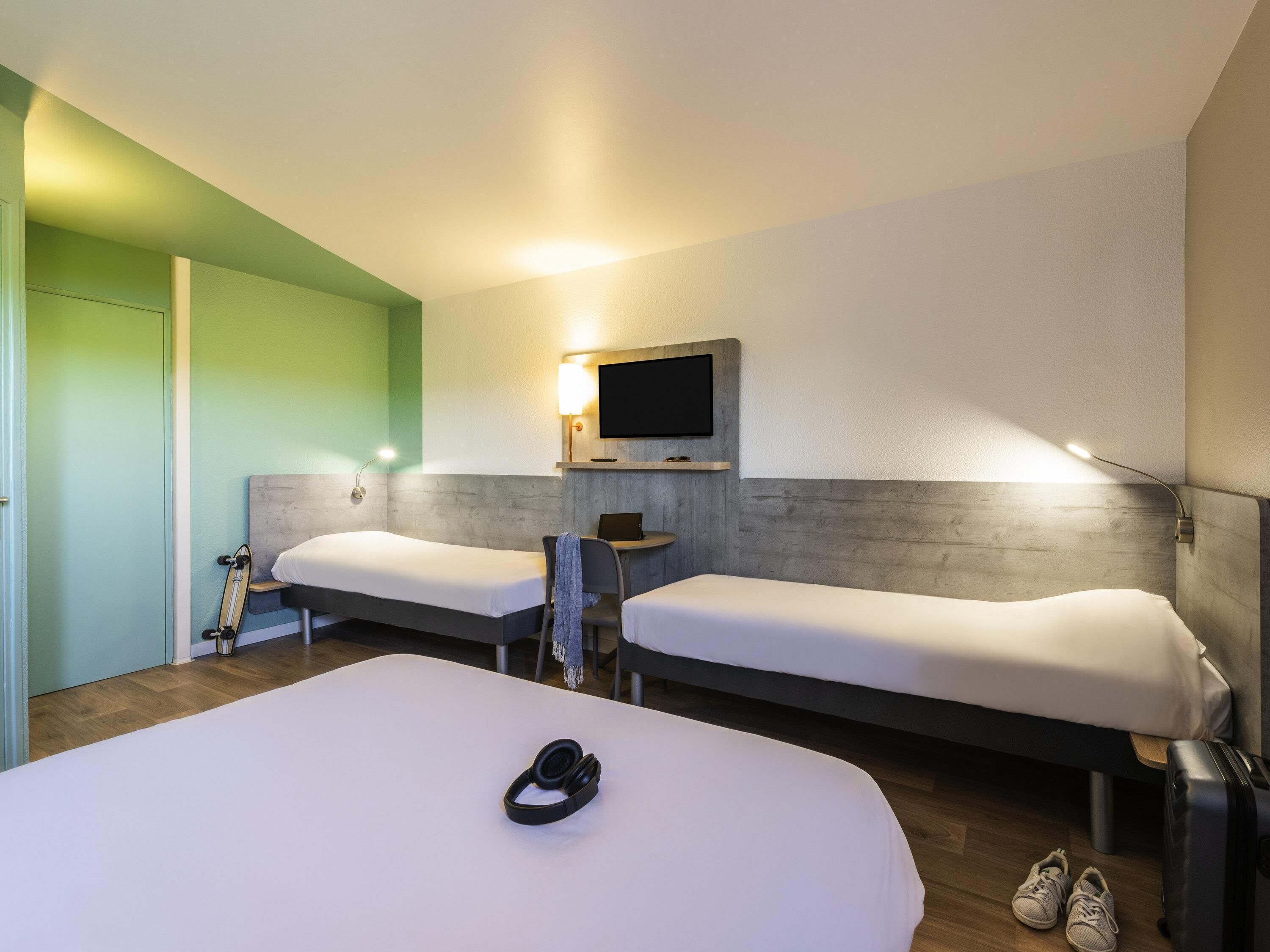 Une chambre d’hôtel avec deux lits, une télévision, un bureau et une valise.