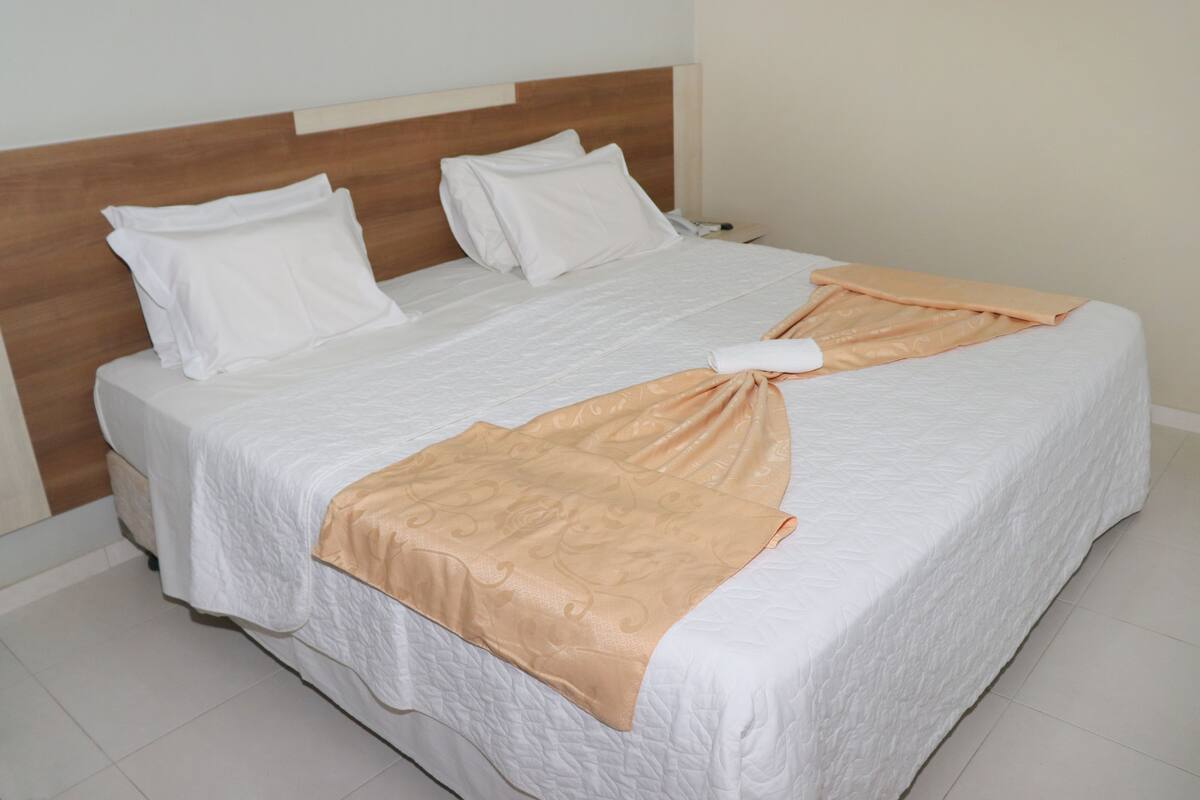 A neatly made bed with white linens and a folded beige blanket.