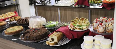 Un buffet proposant une variété de plats, notamment des gâteaux, des pâtisseries et des fruits.