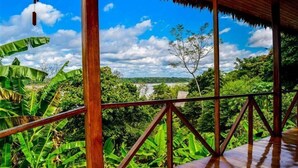 A wooden deck with a view of lush greenery and a river. - Lakshmi Ecolodge and Holistic Spa (Nauta)